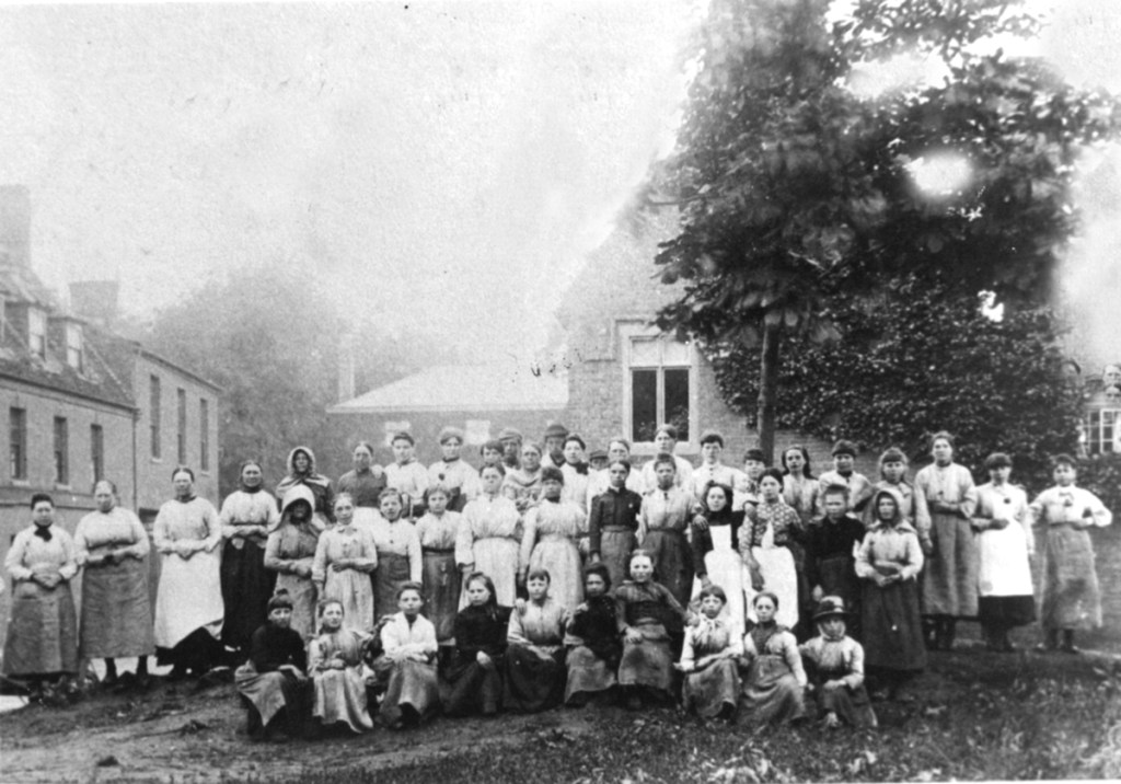 Forty-six people, all but three female, pose for a photograph against a backdrop of buildings on Market Hill, Chatteris. c. 1891